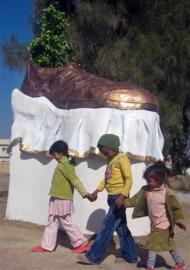 Girls stand next to a sculpture of a shoe that serves as a monument to the shoes thrown at then-US president George W. Bush in Tikrit